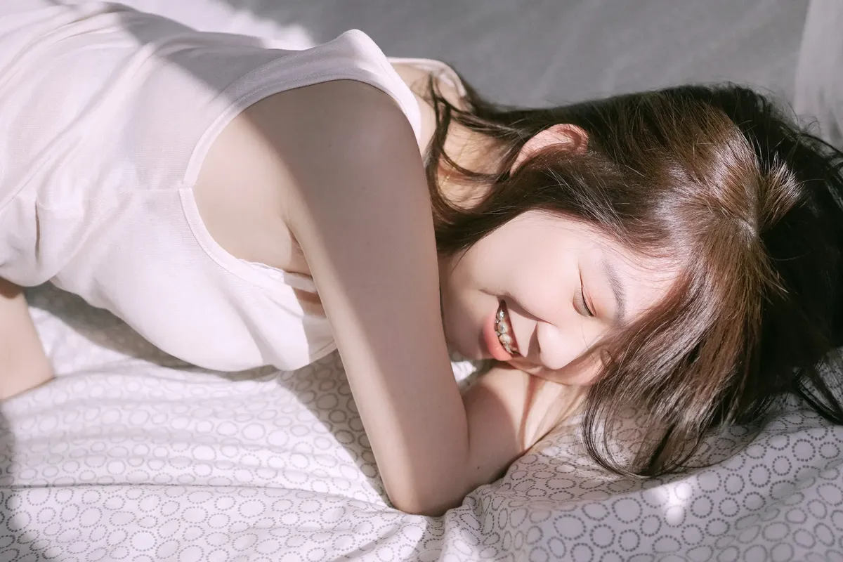 若い女性がベッドで微笑みながら、朝の太陽が窓を通して差し込むのを楽しんでいる。