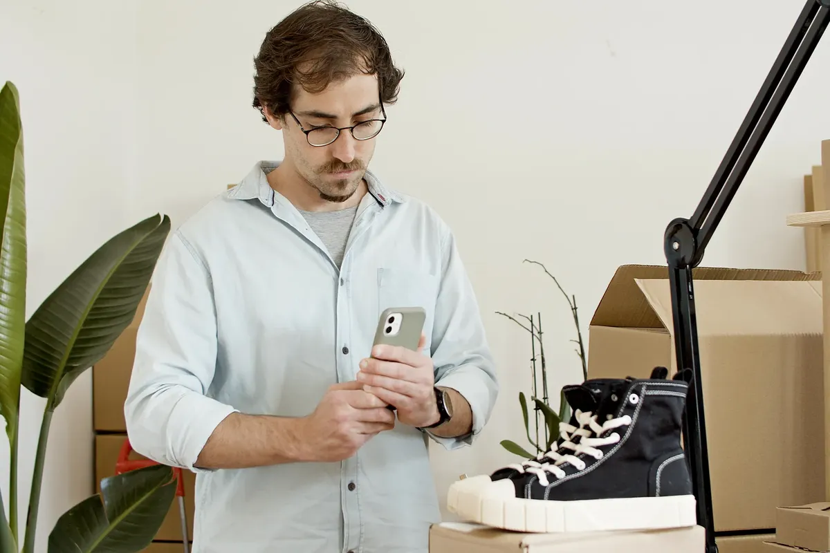 Man uses phone to photograph sneakers in an indoor business setup with boxes.